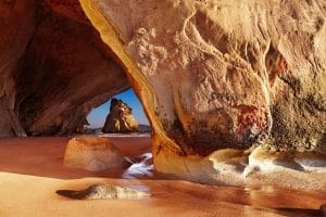 A stunning view of the naturally formed Cathedral Cove in New Zealand, showing clear blue water and rocky cliffs
