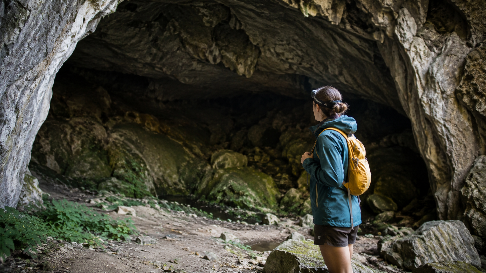 Solo traveler with daypack and headlamp at cave entrance dressed for underground tour adventure