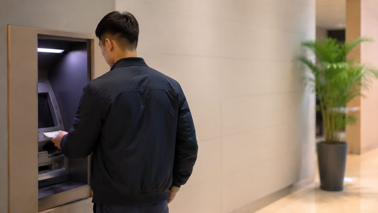 Traveler withdrawing cash from ATM with cautious body language and situational awareness