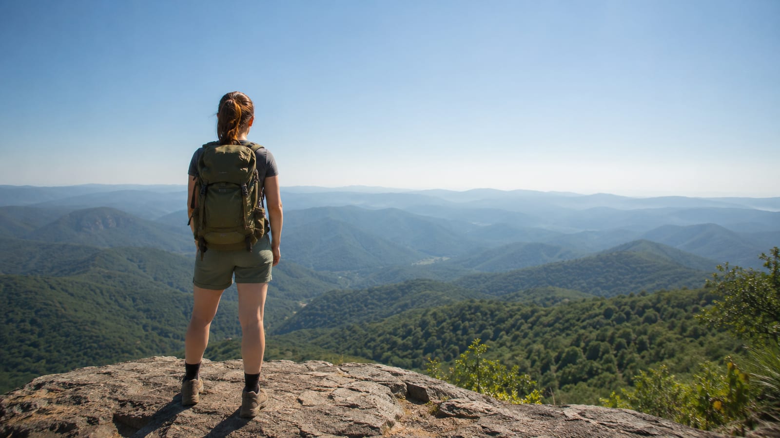Solo traveler with daypack overlooks layered Appalachian mountains beneath a clear autumn sky