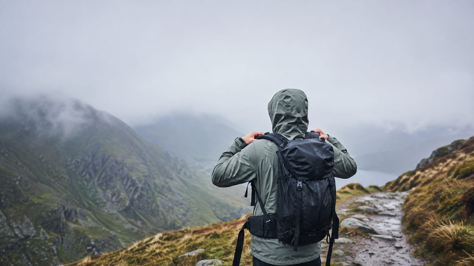 Traveler in rain shell adjusting backpack beside a wet mountain trail