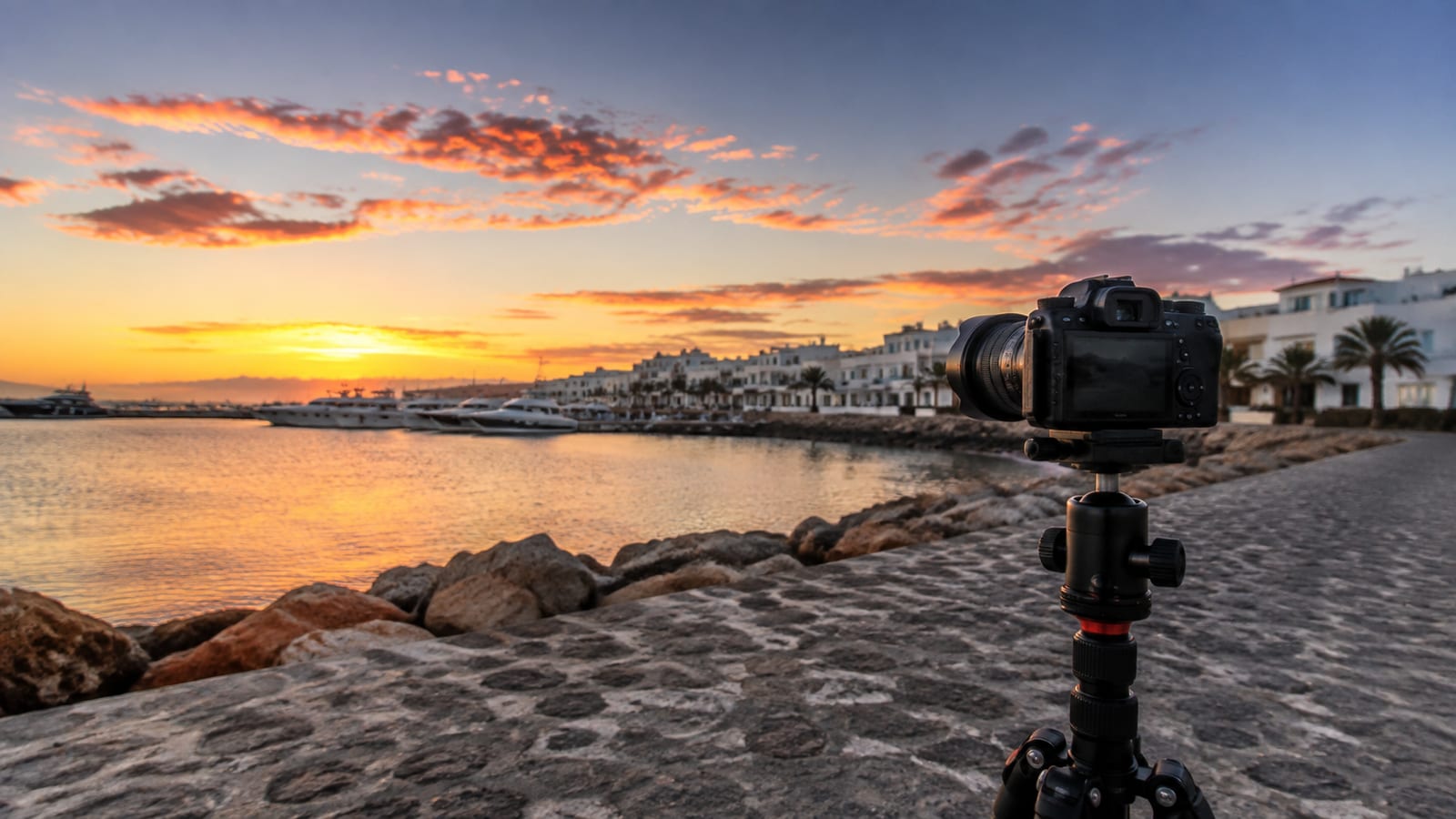 Coastal promenade photographer shooting boats and white architecture beneath dramatic Atlantic evening light