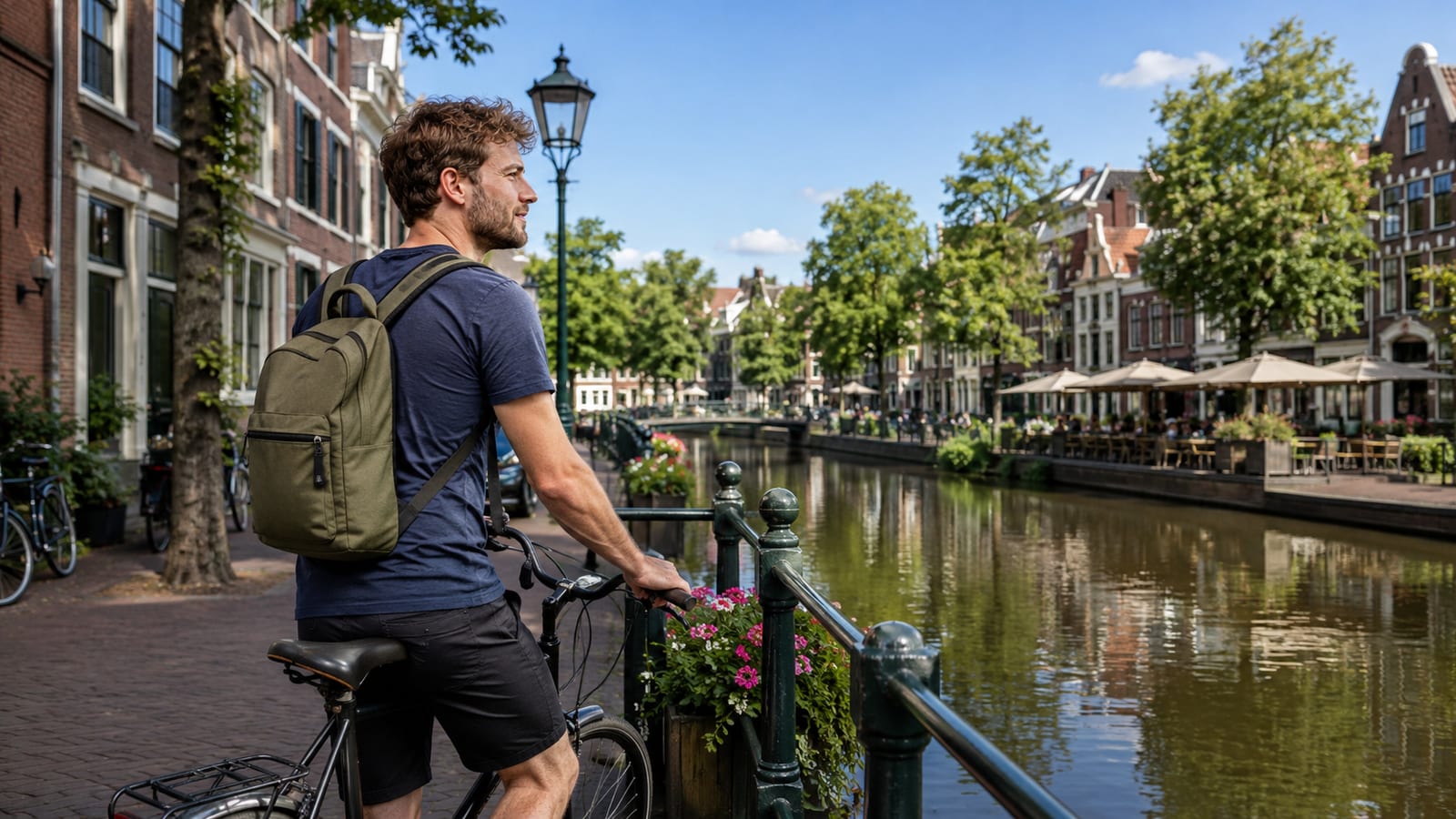 Man wearing a backpack on a bicycle beside a canal lined with historic buildings