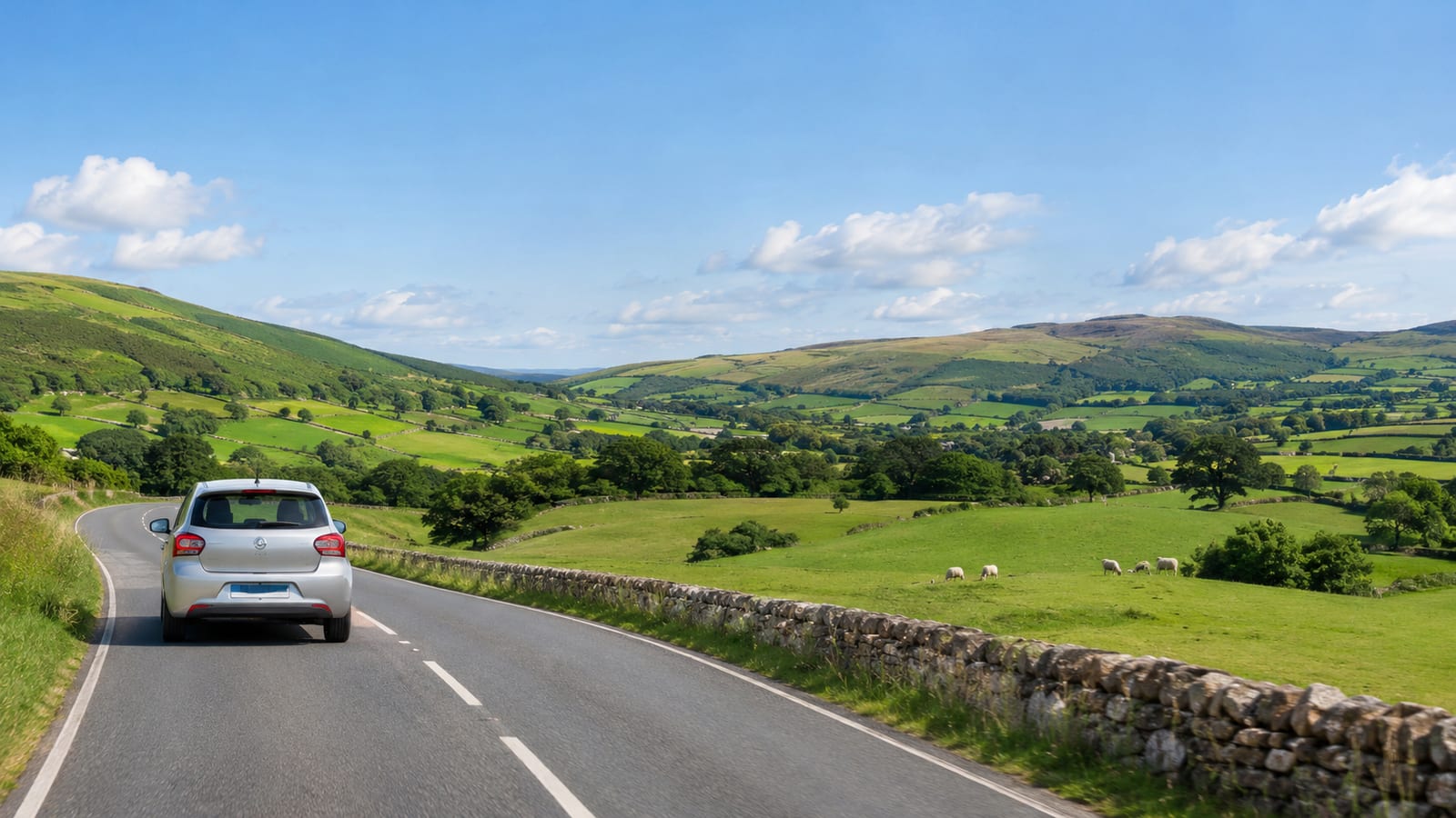 Silver car driving on a winding countryside road past rolling green hills with grazing sheep